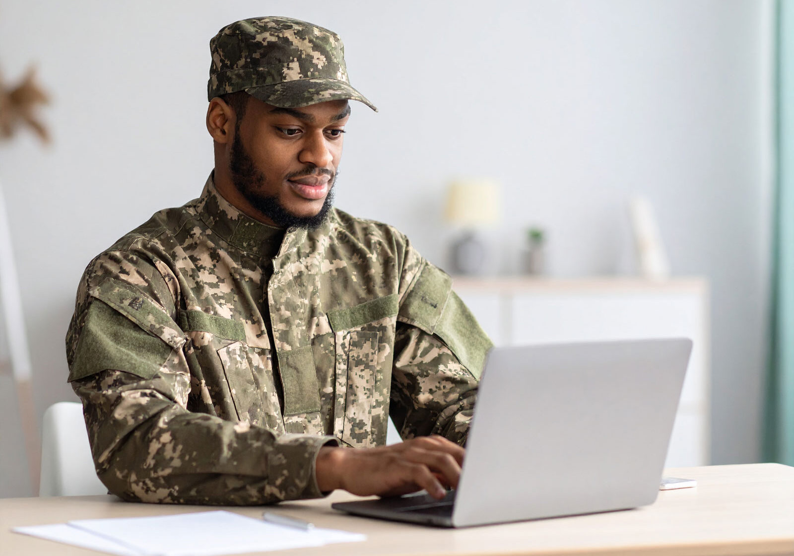 man-on-military-uniform-searching-the-web-on-a-laptop,-seating-on-a-table-at-home